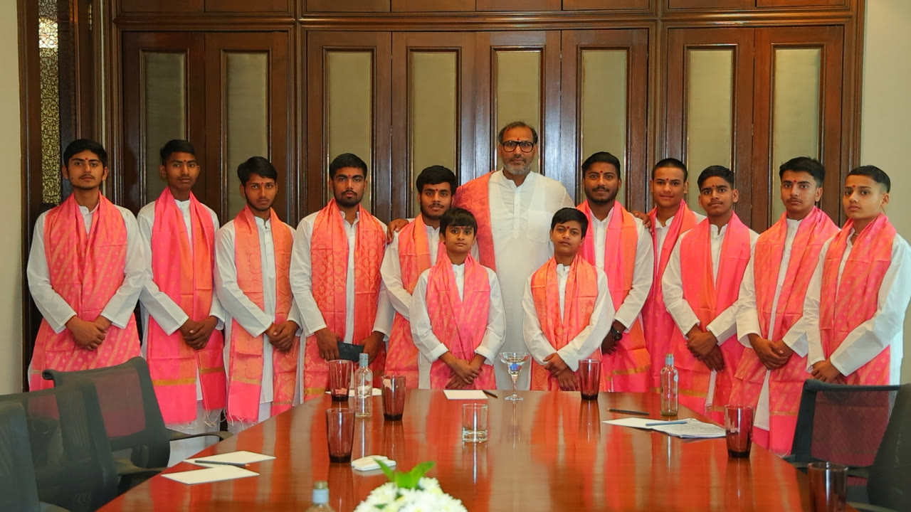 Hemant Acharya with his full group of young pandits, all in white kurtas and rose-gold stoles